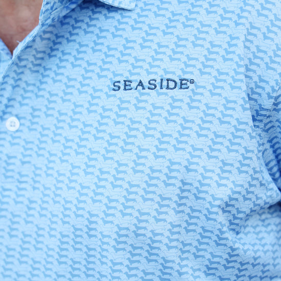 Close-up of a light blue dachshund patterned polo shirt with 'SEASIDE' embroidered on the chest, worn by a model.