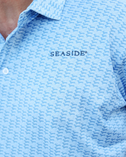 Close-up of a light blue dachshund patterned polo shirt with 'SEASIDE' embroidered on the chest, worn by a model.