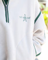 Close-up of a white fleece pullover jacket with green trim, a silver zipper, and 'SEASIDE' embroidered on the chest.