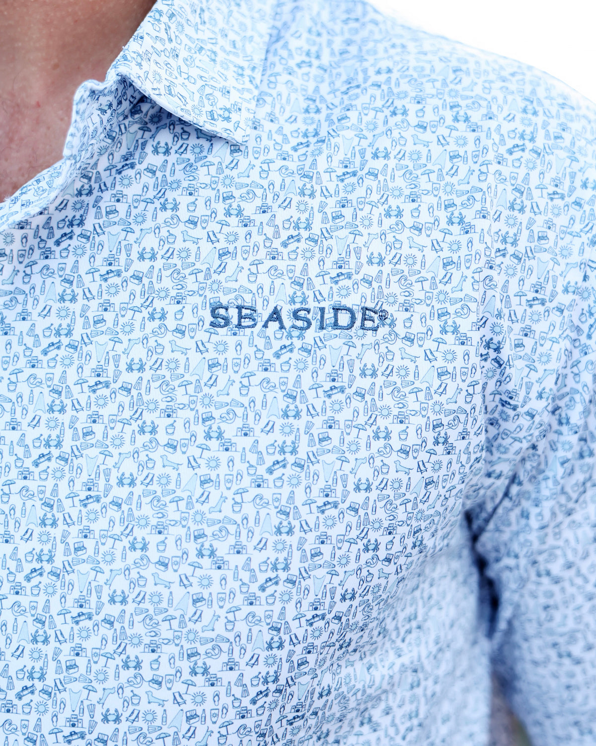 Close-up of a light blue and white patterned button-down shirt with 'SEASIDE' embroidered on the chest, worn by a model.