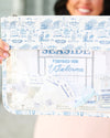 A person holds a clear zip pouch with a blue and white toiletted border. The pouch features a transparent center section displaying various thread and sewing supplies, including spools of thread, a small blue bow, and labels.
