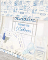 A close-up of a cross-stitch or embroidery fabric design featuring the seaside welcome sign in blue and white. 