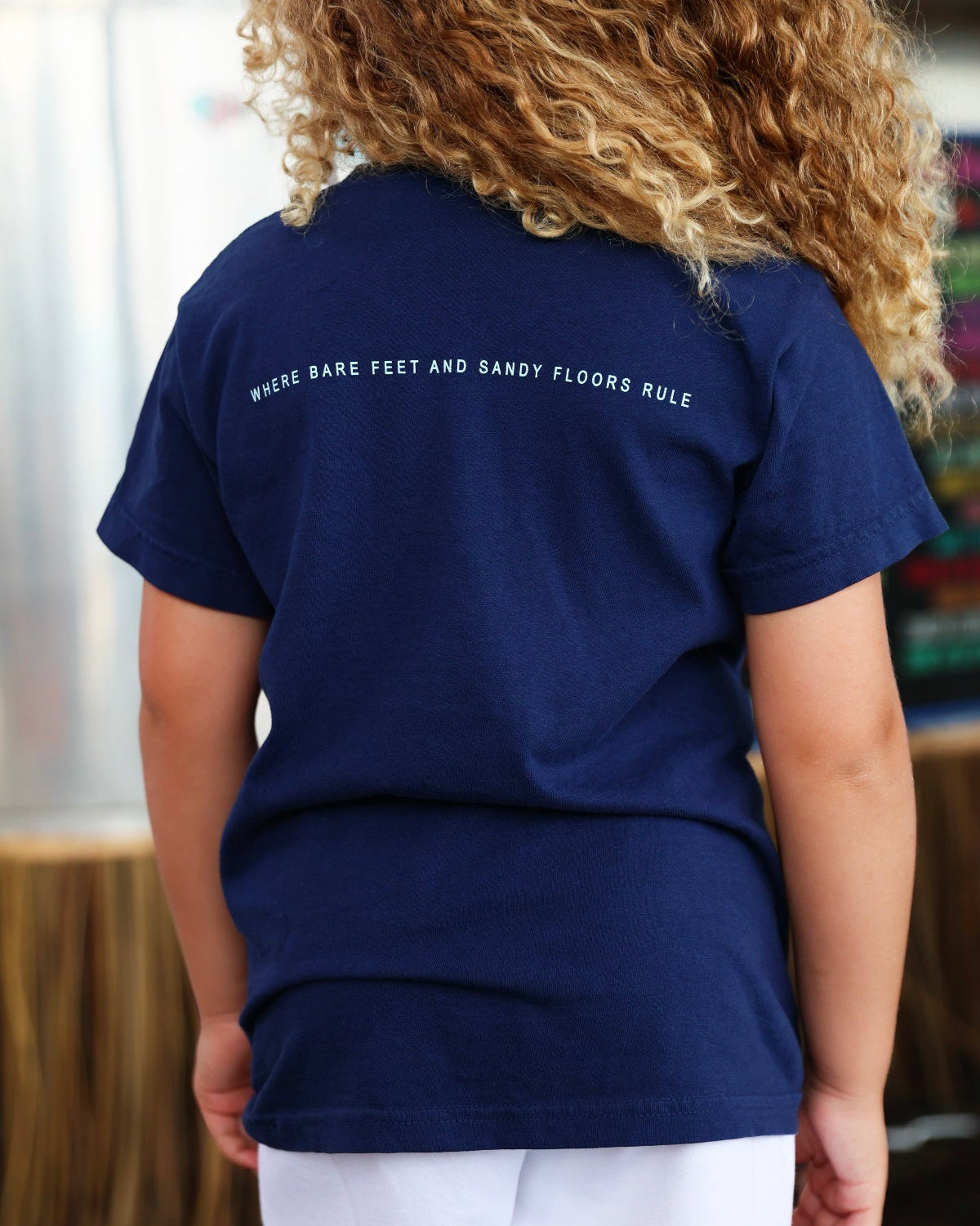 Youth Navy Blue Colors of Seaside Rainbow Tee Back with tagline "where bare feet and sandy floors rule"