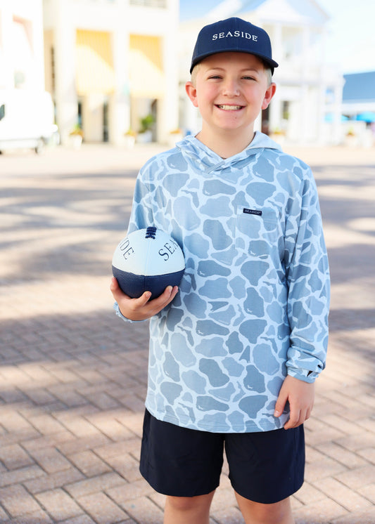 Child wearing a blue patterned hoodie and cap, holding a football with 'Seaside' branding.