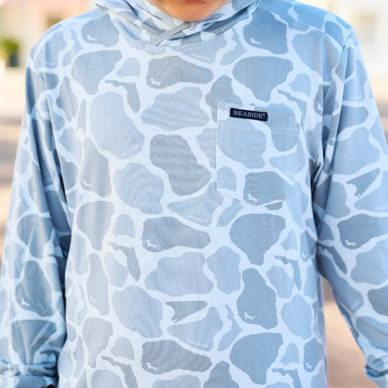 Person wearing a blue camouflage hoodie with a brand logo on a blurred background