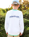 A child viewed from behind wearing a white crewneck sweatshirt with a blue graphic print on the back, khaki pants, and a light blue baseball cap, set against a blurred outdoor background.