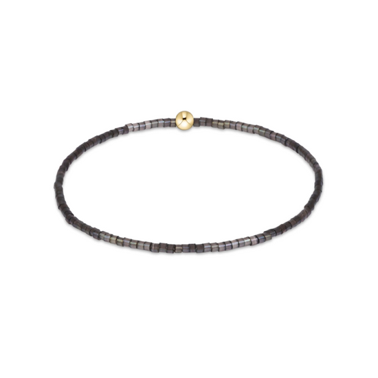 A delicate beaded stretch bracelet with small dark gray and black beads, featuring a single gold-toned round bead at the center, displayed on a clean white background.