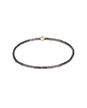 A delicate beaded stretch bracelet with small dark gray and black beads, featuring a single gold-toned round bead at the center, displayed on a clean white background.