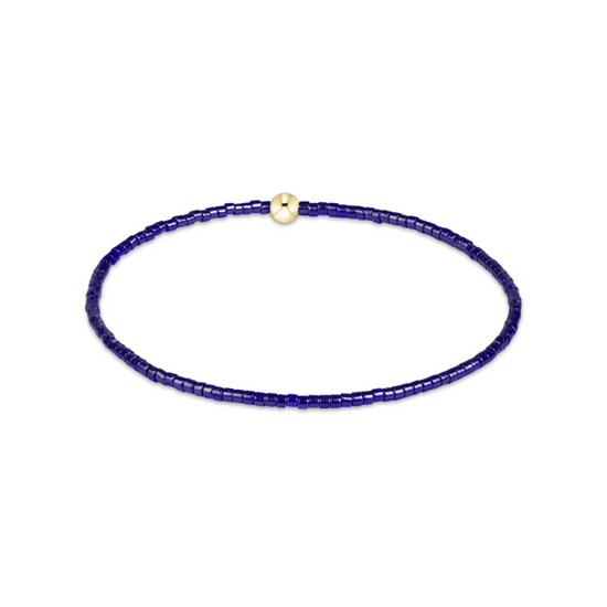 A delicate beaded bracelet composed of small dark blue beads with a single small gold spacer bead, displayed on a clean white background.