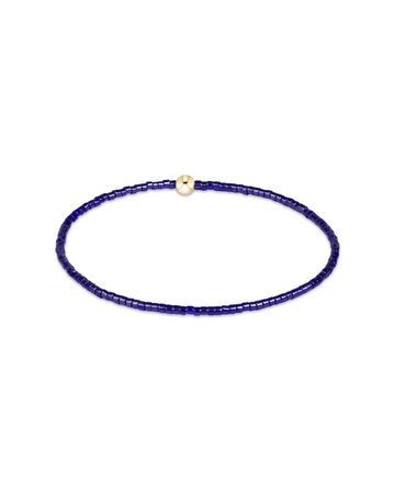 A delicate beaded bracelet composed of small dark blue beads with a single small gold spacer bead, displayed on a clean white background.