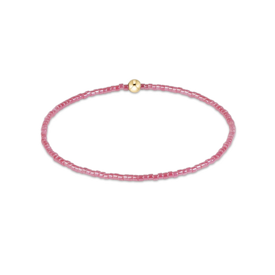 A delicate pink beaded bracelet with a small gold bead accent at the clasp, displayed on a clean white background.